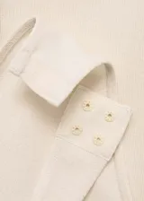 Body de tejido de punto en color beige, con cuello en pico y tirantes anchos. Presenta una hilera de botones decorativos en el frente y un diseño entallado al cuerpo.