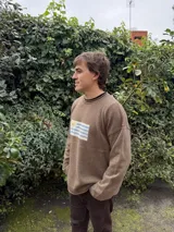 Sweater gris de lana con cuello alto y diseño de la bandera de Uruguay tejida en el frente. Corte clásico y mangas largas.