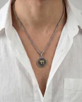 Collar con dije circular de acero inoxidable, con centro esmaltado en negro y símbolo Jai en baño de oro. Incluye cadena de eslabones tipo veneciana.