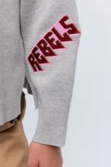 Sweater color camel de tejido de punto con cuello redondo y mangas largas. Presenta bordado de flor en el frente y la palabra 'Rebels' en la manga.