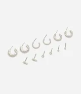 Kit de seis pares de aros plateados de metal, con diseños variados que incluyen aros de argolla con y sin strass, aros tipo botón con piedra brillante, aros de esfera pequeña y aros alargados con cristales.