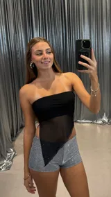 Top strapless negro con diseño asimétrico en el ruedo, confeccionado con una capa superior de tul transparente y una base opaca en el busto.