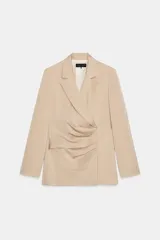 Blazer color beige claro, de corte cruzado con solapa con muescas, hombreras y manga larga. Presenta un detalle de pliegues drapeados en el delantero.