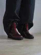Botas de caña media de cuero liso color bordó, con suela gruesa de goma y cierre frontal con tira roja en contraste.