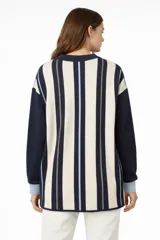 Cardigan de punto con diseño asimétrico, presentando un lado con estampado de rombos en tonos rosa, marrón y blanco, y el otro lado con rayas horizontales en verde oliva y marrón. Posee cuello en V, cierre frontal con botones y mangas largas con puños en contraste.