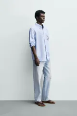 Camisa regular fit de manga larga con diseño a rayas verticales celestes y blancas. Cuenta con cuello abotonado, bolsillo de parche en el pecho y cierre frontal con botones.