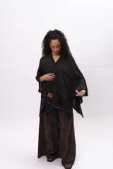 Ruana tejida de punto en mezcla de algodón y lurex, con acabado brillante. Presenta un diseño holgado con escote en V y etiqueta de cuero sintético con logo de la marca en el frente.