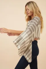 Poncho color beige con diseño a cuadros, cuello bote y terminaciones desflecadas. Tiene aberturas para los brazos en los laterales y detalles en cuero.