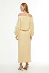 Falda midi color amarillo pálido, de corte recto con abertura frontal y cinturón con hebilla circular.