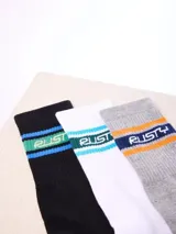 Pack de tres pares de medias largas tipo crew de la marca Rusty, en colores negro, blanco y gris melange, con diseño de franjas de colores y el nombre de la marca en el centro.
