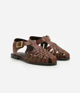 Sandalias planas de cuero marrón con tiras entretejidas, hebilla dorada y suela negra.