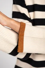 Sweater de punto con diseño a rayas horizontales en color negro y crema, de corte oversize. Presenta cuello redondo, mangas largas con puños acanalados y un detalle de borde inferior en color cobre con acabado brillante.