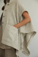 Capa de lana fina con cuello alto, cierre frontal con botones ocultos y bolsillos plaqué. Presenta aberturas laterales versátiles que permiten usarla como poncho o ruana, con terminaciones envivadas.