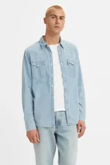 Camisa de denim celeste claro, corte clásico, con cuello americano, cierre frontal con botones a presión, dos bolsillos con solapa abotonada en el pecho y mangas largas con puños abotonados.