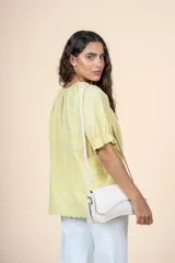 Blusa amarilla pastel de algodón con textura delicada, escote redondeado con lazo, mangas cortas abullonadas con volados y terminaciones sutiles.