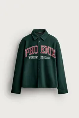 Sobrecamisa verde oscuro de corte relaxed fit con cuello solapa, manga larga con puño abotonado y cierre frontal de botones. Cuenta con bordados combinados a contraste en el delantero con la inscripción "PHOENIX WORLDWIDE GOODS".