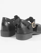 Mocasín tipo sandalia de cuero vegano color negro, con diseño calado en la parte frontal, cierre con hebilla lateral y taco bajo cuadrado.