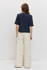 Pantalón de jean wide leg color beige con pequeños bordados y estampados coloridos dispersos, de tiro medio y corte amplio en las piernas.