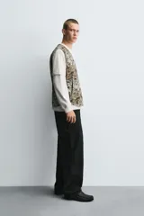 Chaleco acolchado de algodón con cuello pico y cierre frontal de cremallera. Presenta un estampado abstracto en tonos tierra y gris, con bolsillos de vivo en la cadera.