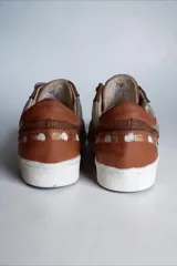 Sneakers de cuero marrón con detalles en cobre, paneles texturizados, talón plateado y suela blanca.