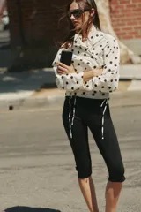 Chaqueta blanca con estampado de lunares negros, cuello subido ajustable con cordón, cierre frontal con botones y bajo ajustable con cordones.