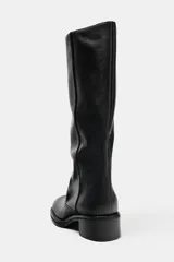 Bota alta de piel estilo biker, color negro, con diseño slouchy y puntera semi cuadrada. Cuenta con tacón bajo y ancho.