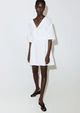 Vestido corto blanco de algodón con diseño broderie, escote en V con solapa, mangas cortas abullonadas y cintura elástica fruncida.