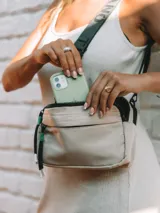 Bandolera de lona color beige, con diseño compacto de dos compartimentos con cierre. Incluye correa ajustable y tiradores con cordones decorativos.