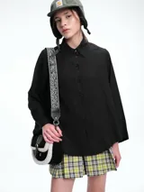 Camisa de corte oversize color bordó, con cuello clásico, cierre frontal de botones y mangas largas amplias con puños anchos. Presenta un diseño de caída fluida con bajo redondeado y levemente más largo en la parte posterior.