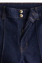 Jean de tiro alto en denim azul oscuro con pierna amplia y corte tobillero. Presenta un diseño de cinco bolsillos, cierre frontal con botón y costuras decorativas verticales en el frente que simulan un pliegue.