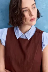 Top blanco sin mangas, con cuello redondo, diseño cruzado en el frente y cierre con botones en el hombro.