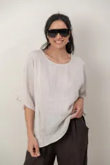 Blusa de lino color marrón oscuro, con escote redondo, mangas cortas amplias y detalle de alforzas verticales en el lateral derecho.