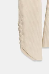 Chaqueta de punto color crema, con cuello redondo, manga larga abullonada en el hombro y acabado asimétrico en el puño. Cierre frontal con botones.
