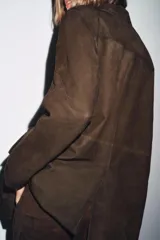 Blazer de mujer color marrón oscuro, confeccionado en piel de ante 100%. Presenta cuello solapa de muescas, manga larga, bolsillos de plastrón frontales y cierre frontal de botones.