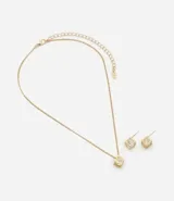 Conjunto de bijouterie compuesto por un collar de cadena fina con dije cúbico calado y aros tipo stud a juego, ambos con incrustaciones de cristal.