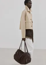 Chaqueta corta de algodón en color beige, con cuello camisero, mangas largas, dos bolsillos con solapa en el frente y cierre de botones.