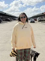 Canguro amarillo de corte holgado con capucha y cordones ajustables. Presenta el logo bordado en color marrón en el centro del pecho y un bolsillo frontal tipo canguro.