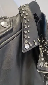 Campera estilo motoquera de símil cuero negro, con solapas amplias y detalles de tachas metálicas en solapas, hombros y mangas. Presenta cierre frontal cruzado, bolsillos con cierre y trabillas en el ruedo.