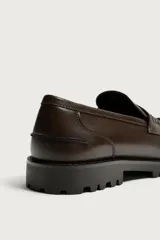 Mocasín de vestir negro con capellada lisa, detalle de antifaz en el empeine y suela track robusta.