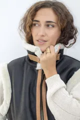 Chaleco estilo bomber de cuero negro con interior y detalles de piel sintética en color crema. Presenta cierre frontal con solapa de cuero en tono tostado y mangas de tejido de punto color crema.