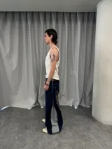 Pantalón de jean azul raw con diseño de corte versátil, ajustable mediante cierres laterales que revelan un panel interior rojo. Presenta una estampa gráfica de gran tamaño en la parte trasera con detalles bordados, costuras reforzadas y etiqueta de cuero en la cintura.