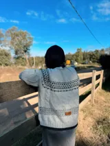 Sweater de punto en color marrón con diseño jacquard geométrico en blanco y gris en cuello, puños y pecho. Presenta cuello redondo, mangas largas y corte holgado.