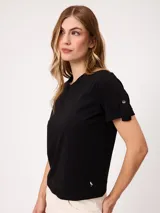 Remera blanca de manga corta con vuelta en los puños y detalle de botón dorado. Presenta cuello redondo y corte recto.