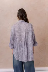 Camisa lila oversize de algodón con bordado floral calado tipo broderie, cuello camisero, manga larga y abotonadura frontal.