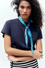 Pañuelo o bandana de seda y algodón, color fucsia intenso, con estampado floral y paisley en tonos beige/crema. Se anuda al cuello con un broche metálico en forma de corazón dorado y verde.