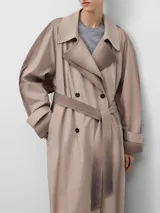 Gabardina cruzada color beige con efecto envejecido, de corte recto y largo midi. Presenta doble solapa en el lado derecho, doble botonadura frontal, bolsillos laterales, mangas largas con trabillas en los puños y canesú amplio en la espalda.
