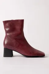 Bota de caña media con textura de reptil en color bordó, con taco cuadrado negro y punta cuadrada.