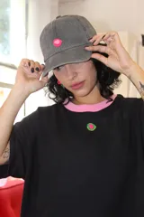 Gorra tipo baseball de color gris con efecto desgastado, presenta un detalle circular en color rosa y verde en la parte frontal.