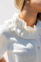Camisa blanca de manga larga con cuello con volados y cierre frontal de botones.