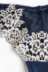 Pack de dos bombachas tipo brazilian de tiro bajo, confeccionadas en encaje floral bicolor azul marino y crema con detalles de malla y pequeño lazo decorativo en el centro.